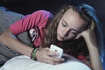 Ein Mädchen liegt am Abend mit ihrem Handy im Bett